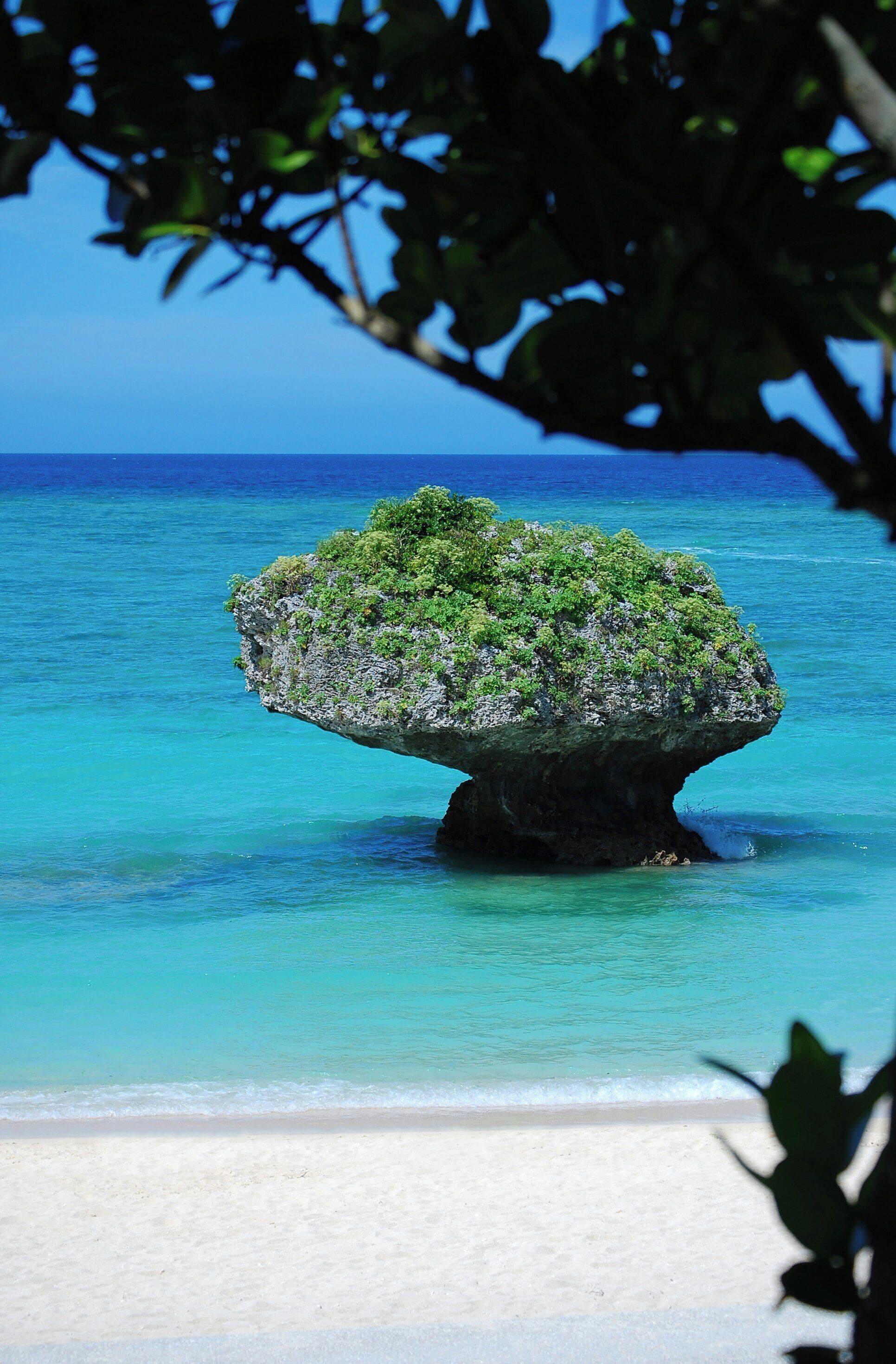 Vista despejada de una playa con una formación rocosa destacada, rodeada de aguas turquesas.