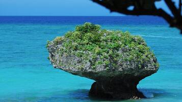 Vista despejada de una playa con una formación rocosa destacada, rodeada de aguas turquesas.