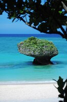 A clear view of a beach with a prominent rock formation surrounded by turquoise water.