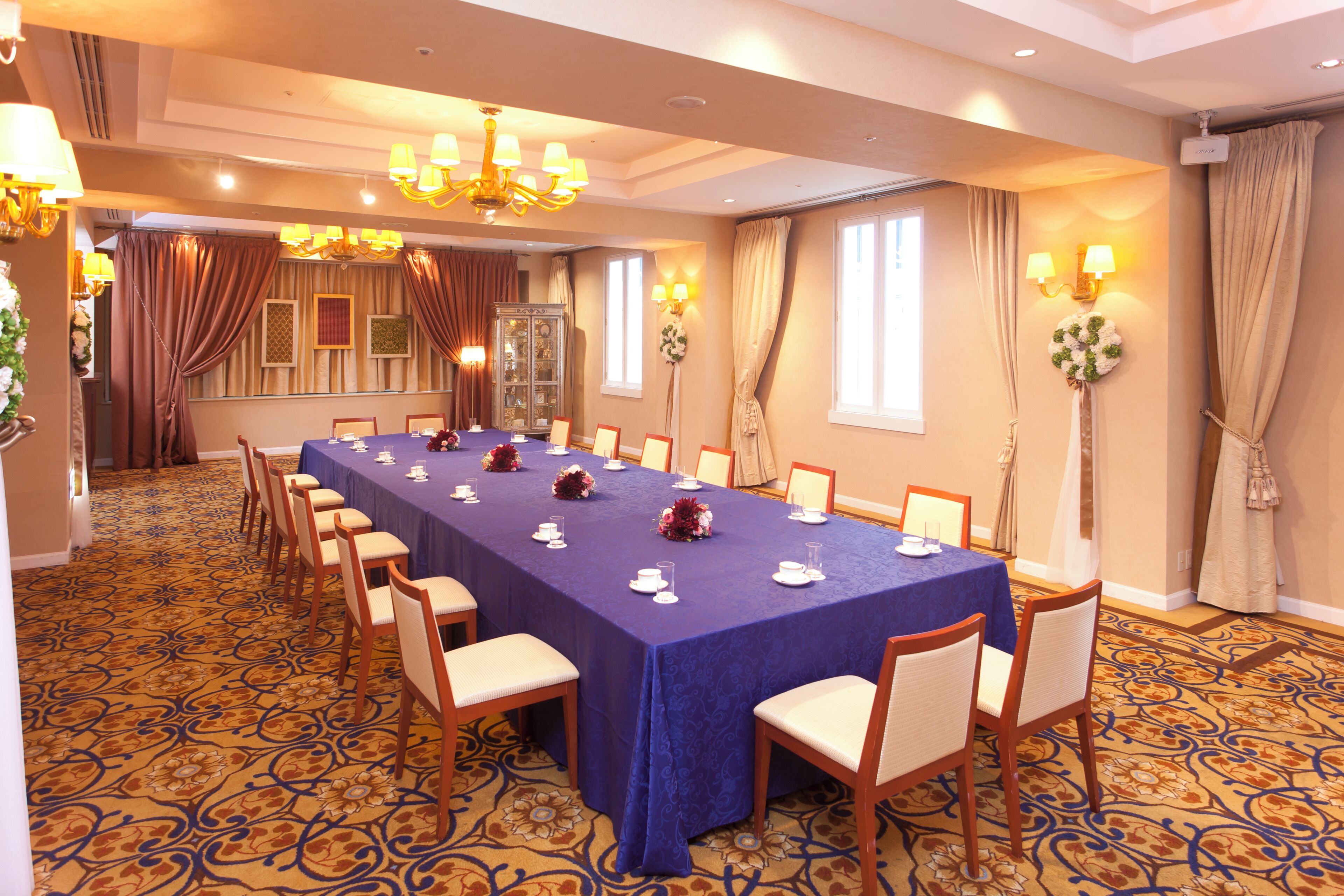 Une salle de conférence avec une longue table, des chaises, des lustres et des appliques murales.