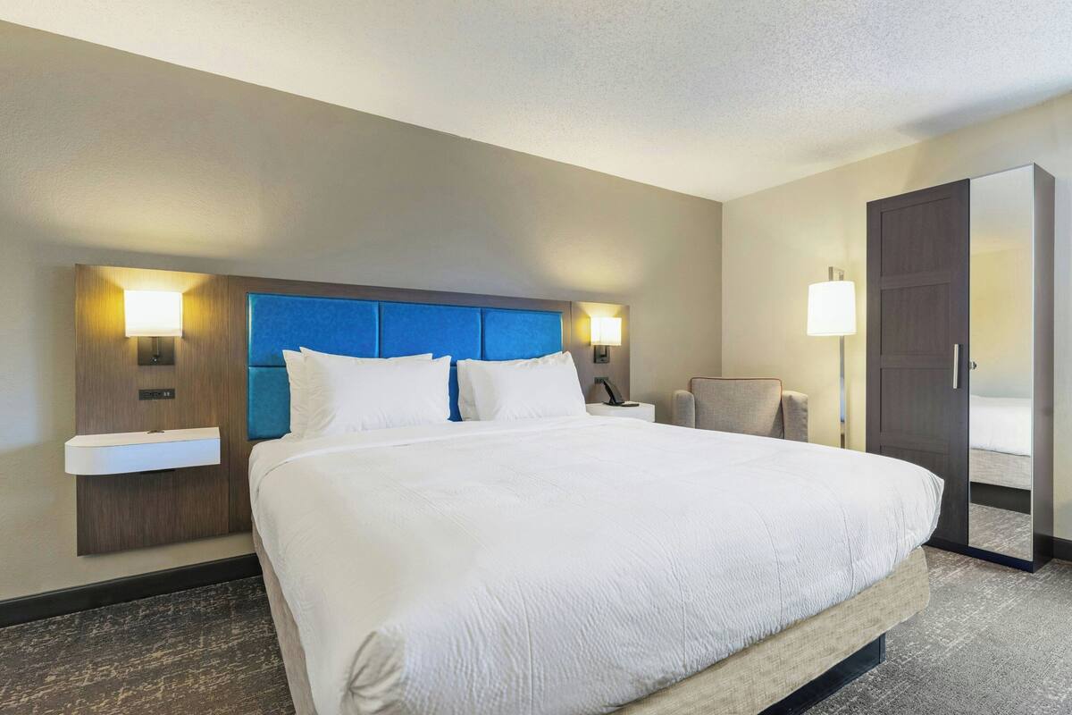 A hotel room with a large bed, bedside tables, a chair, and a wardrobe.