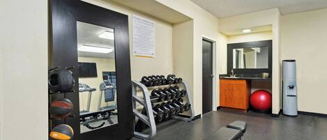 A gym with exercise equipment, a bench, a mirror, and a red exercise ball.