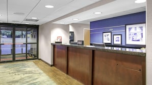 A reception desk with a blue wall and framed pictures, a "welcome to elgin" sign, and a "Hilton" sign. - Elgin Inn (Elgin)