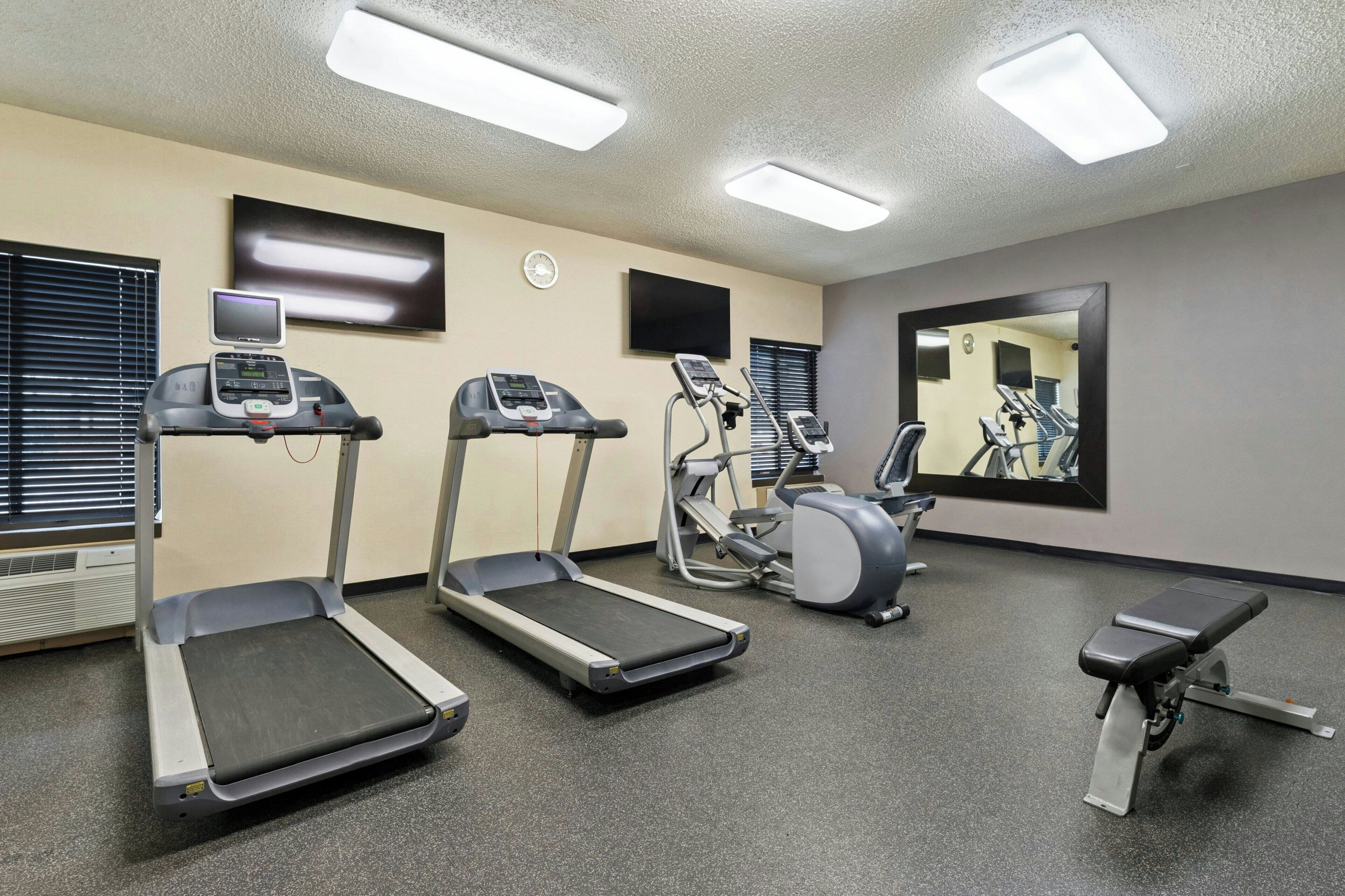 Une salle de sport équipée de tapis de course, d’un appareil elliptique et d’un banc de musculation.