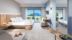 A modern hotel room with a large bed, a desk, a chair, and a view of the beach. - Aeolos Beach Hotel (Kos)
