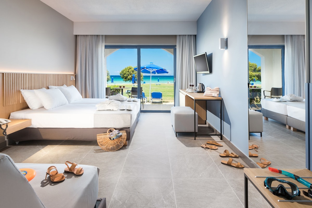 A modern hotel room with a large bed, a desk, a chair, and a view of the beach.
