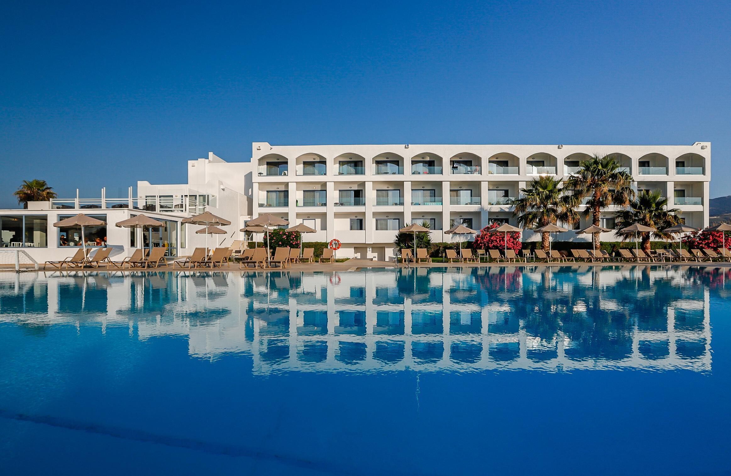 A hotel with a large swimming pool, sun loungers, and palm trees.