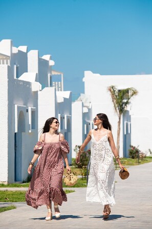 Two women walking on a paved path with white buildings in the background. - Aeolos Beach Hotel (Kos)