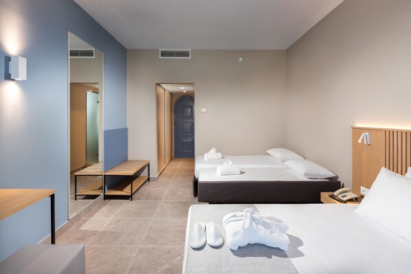Una habitación de hotel con cama, mesita de noche, espejo, banco y puerta que da a otra habitación.