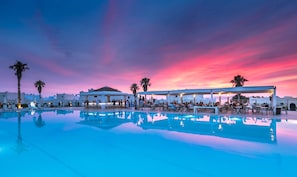 A poolside area with lounge chairs and umbrellas, a bar, and a sunset view. - Aeolos Beach Hotel (Kos)
