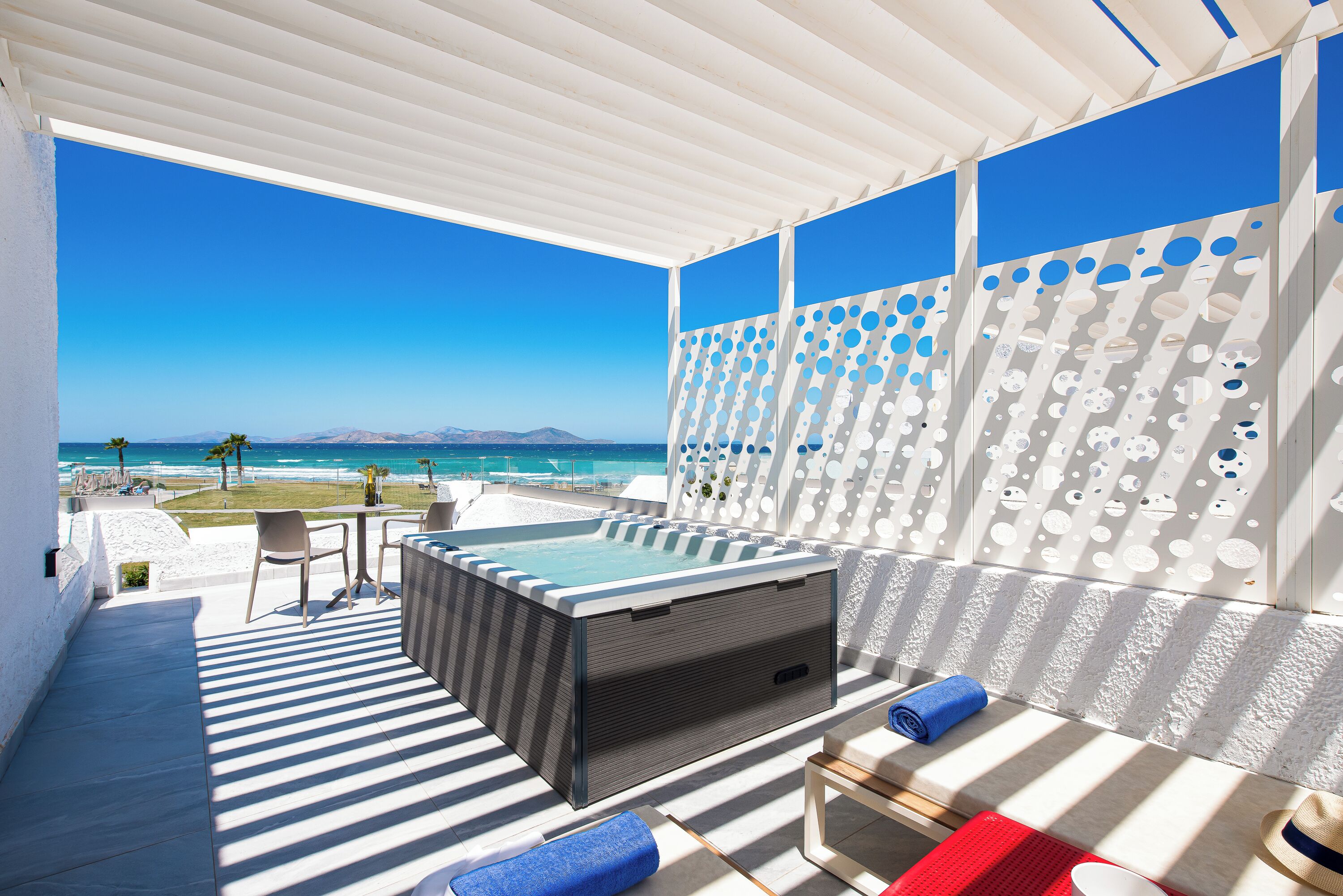 A modern outdoor lounge area with a hot tub, striped flooring, and a view of the ocean.