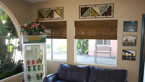 A living room with a brown leather sofa, a beverage vending machine, and two windows with blinds. - Bay Inn and Suites at Seaworld (San Diego)