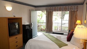 A hotel room with a bed, a television, a minibar, and a window with curtains. - Bay Inn and Suites at Seaworld (San Diego)