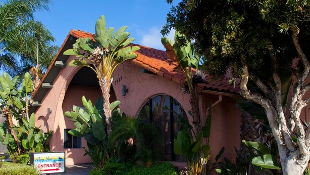 A building with a pink facade, a red-tiled roof, and a large arched entrance. - Bay Inn and Suites at Seaworld (San Diego)