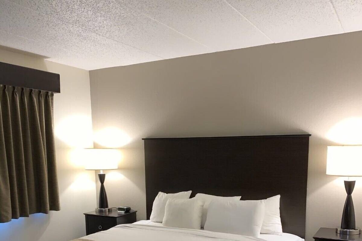 A hotel room with a large bed, two bedside tables with lamps, a dark headboard, and a window with curtains.