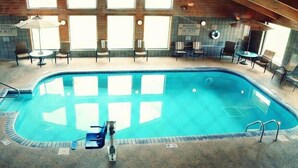Piscina interior con un cartel de servicio de socorrista, rodeada de sillas y mesas.