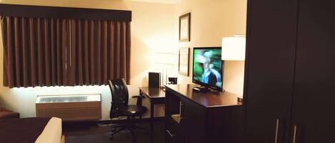 A hotel room with a bed, desk, chair, television, and wardrobe.