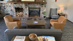 Un hall con chimenea de piedra, dos sillones de cuero, una mesa de centro de madera con revistas y una alfombra estampada.