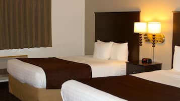 Quarto de hotel com duas camas, uma mesa de cabeceira com abajur e uma janela com cortinas.