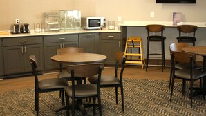 Habitación de hotel con kitchenette, televisor de pantalla plana montado en la pared y zona de estar con mesa redonda y sillas.