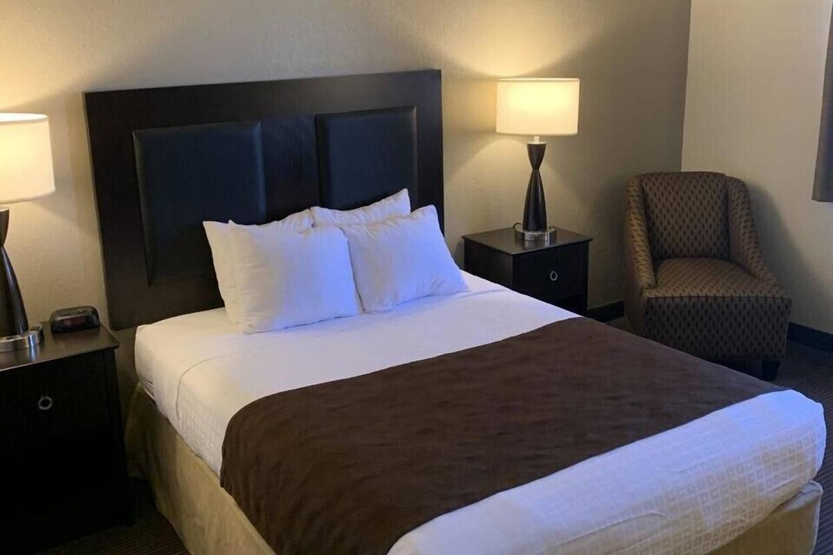 A hotel room with a large bed, two bedside tables, a chair, and a lamp.