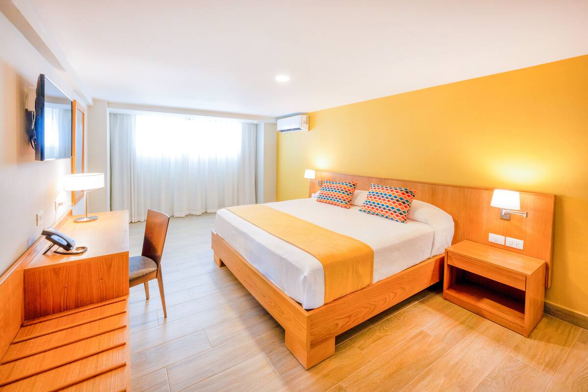 Une chambre d’hôtel avec un lit en bois, un bureau avec un téléphone, une chaise et un téléviseur fixé au mur.