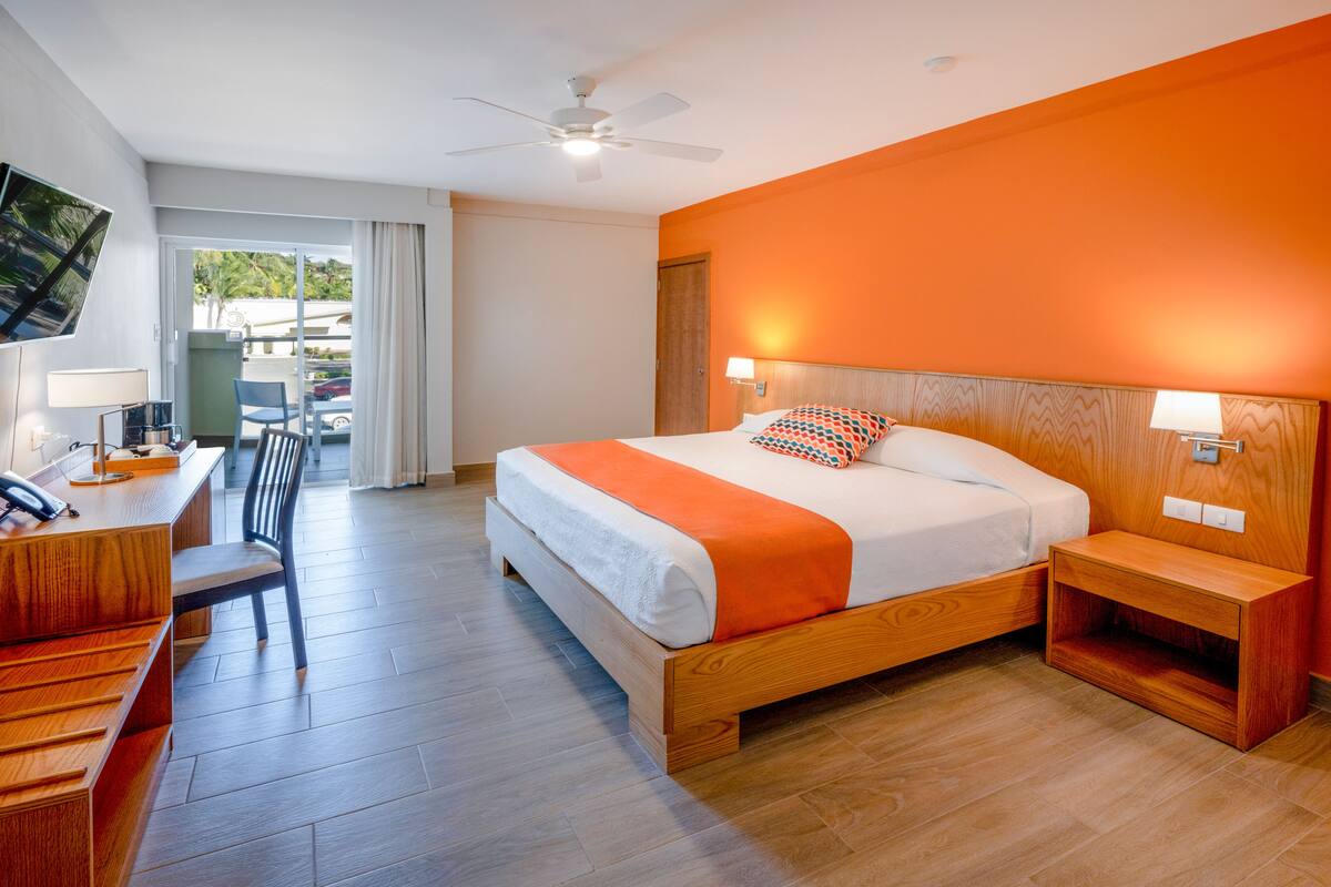 Une chambre d’hôtel comprenant un lit, un bureau avec une chaise, une télévision et un balcon donnant sur l’extérieur.
