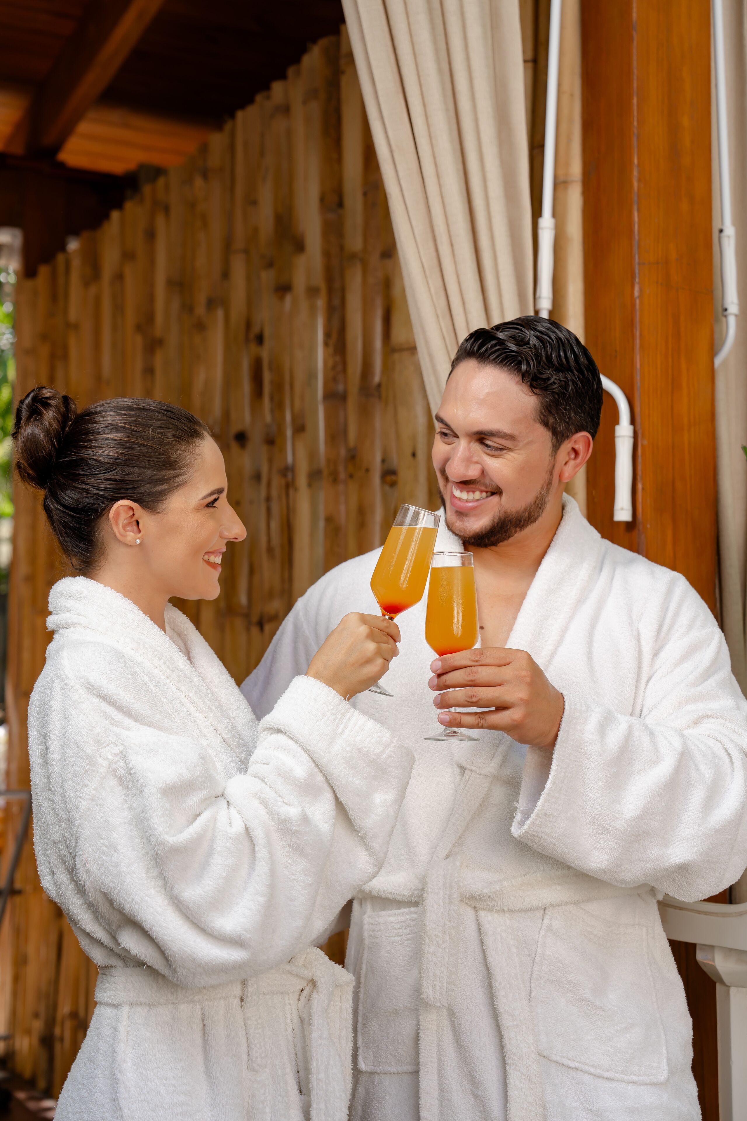 Two people in white bathrobes holding glasses of orange juice.