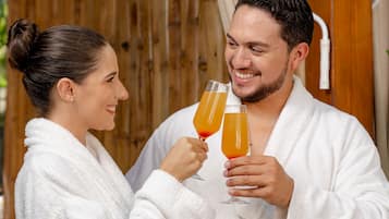 Two people in white bathrobes holding glasses of orange juice.