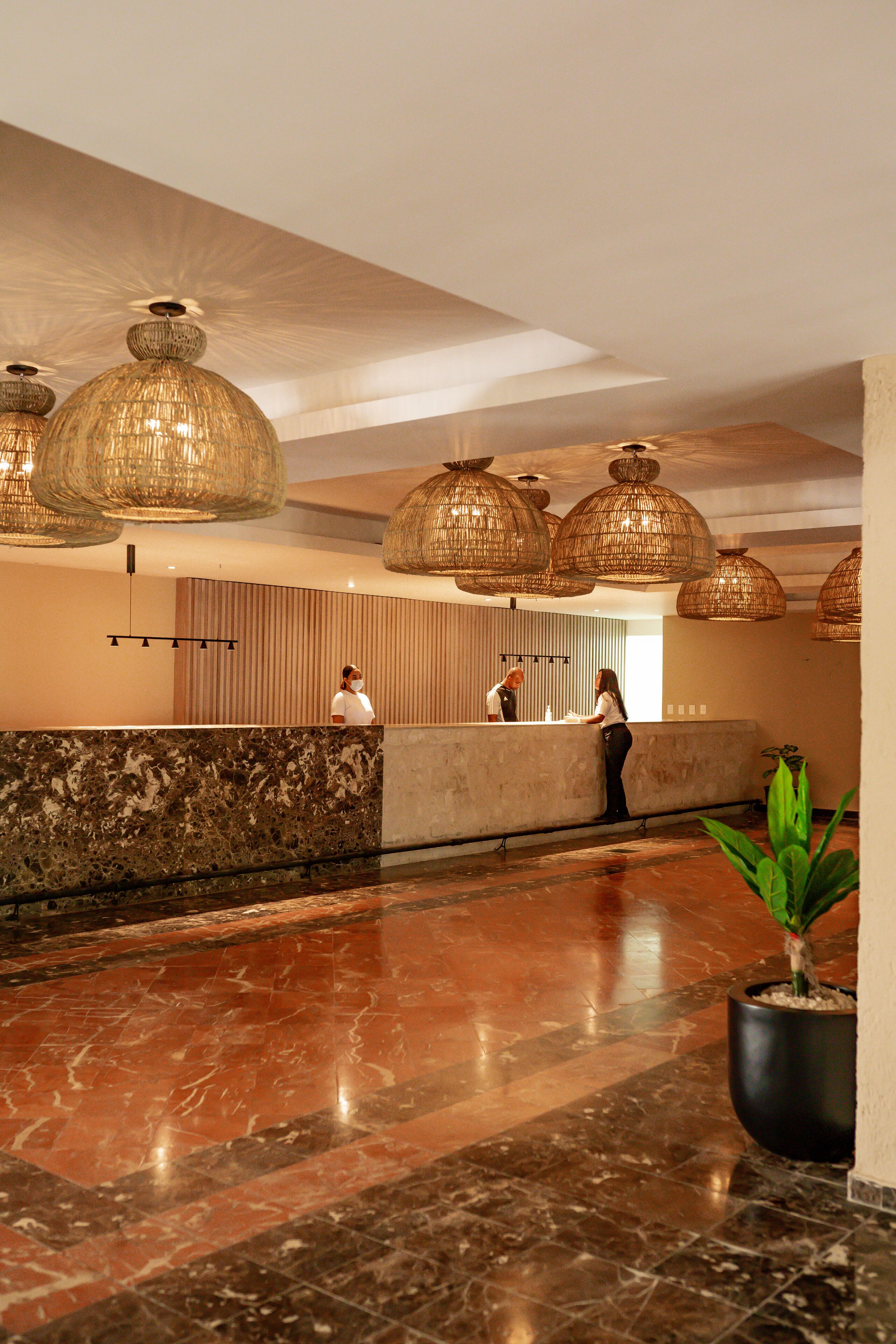 A lobby with a reception desk, large hanging wicker lamps, and a marble floor.