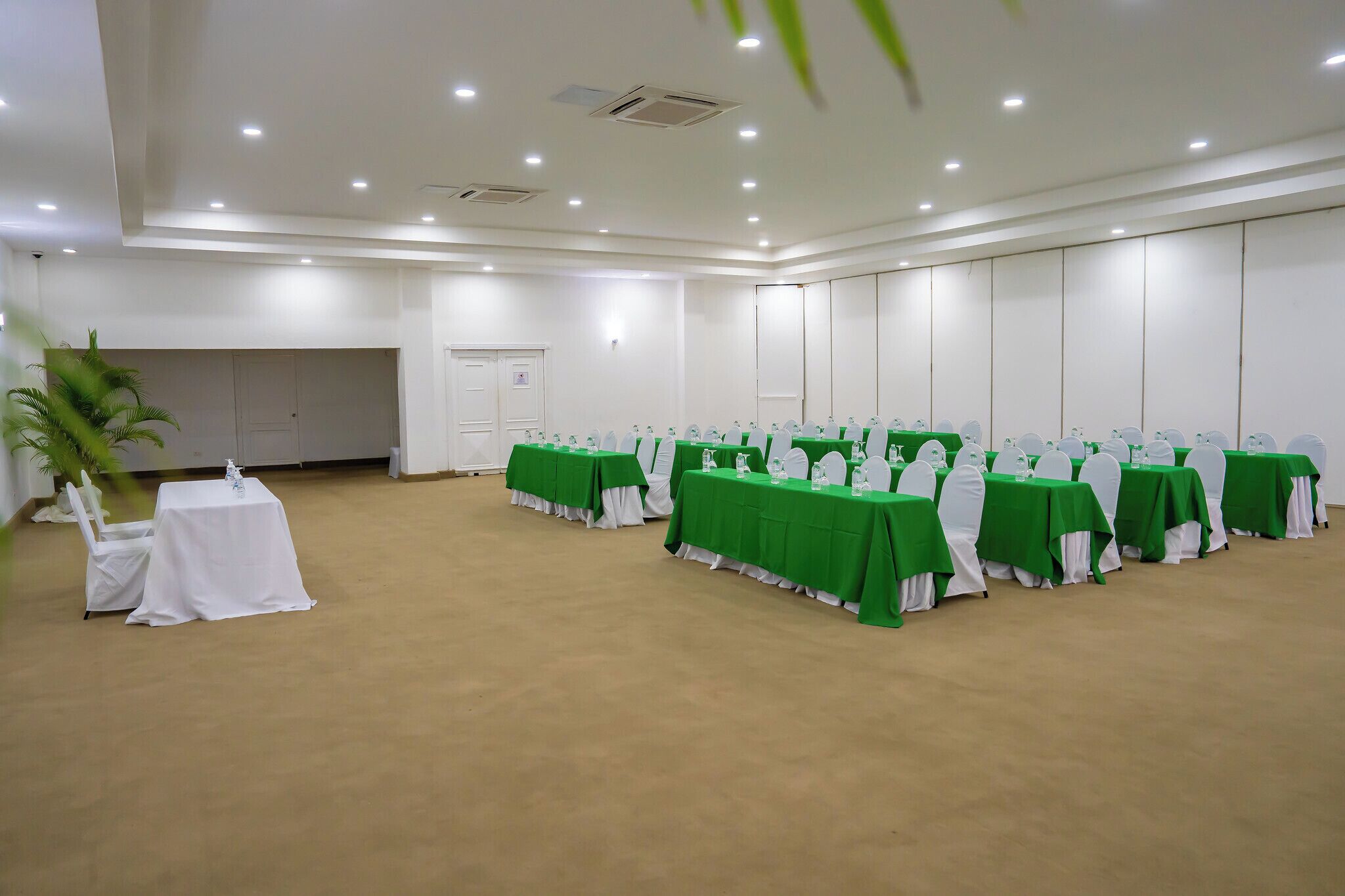 Une salle de conférence dotée de tables vertes et de chaises blanches, équipée de plaques nominatives et de bouteilles d’eau.