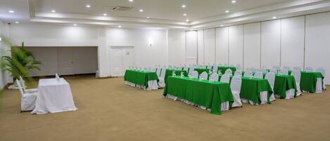 Une salle de conférence dotée de tables vertes et de chaises blanches, équipée de plaques nominatives et de bouteilles d’eau.
