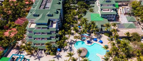 Vista aérea de un resort con varias edificaciones, piscina y palmeras.