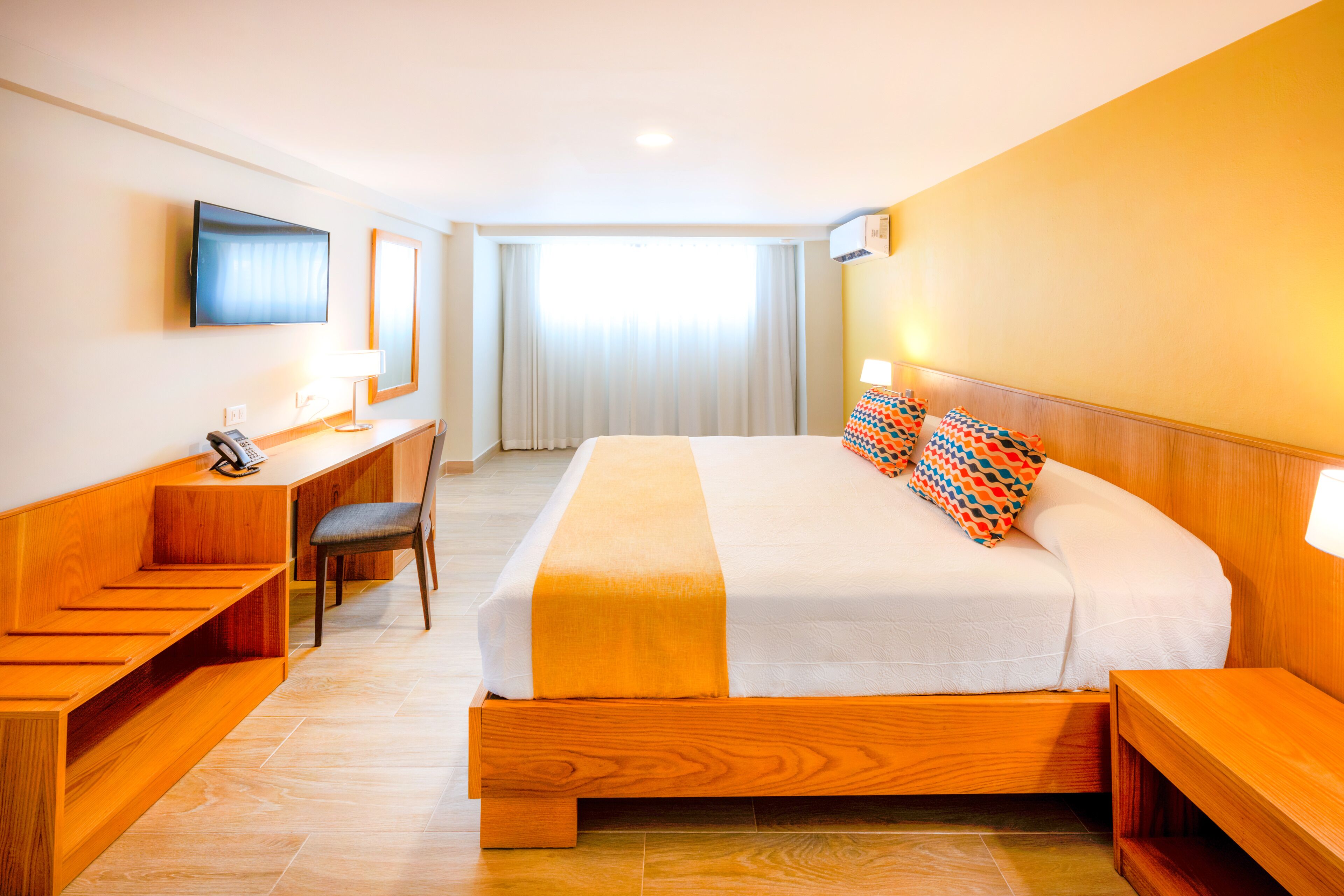 A hotel room with a large bed, wooden furniture, a desk, and a television on the wall.