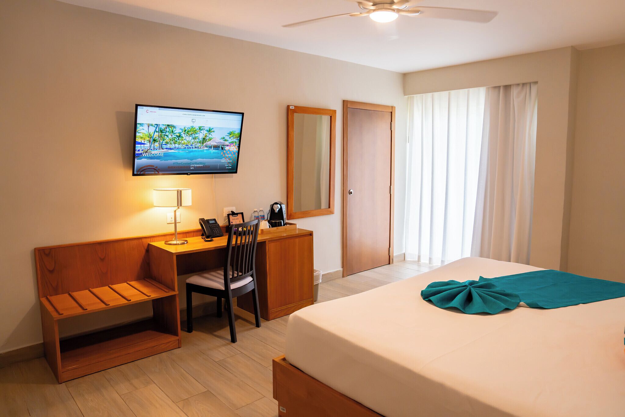 Une chambre d’hôtel comprenant un lit, un bureau avec une chaise, un téléviseur fixé au mur et une fenêtre avec des rideaux.