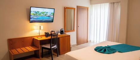 Une chambre d’hôtel comprenant un lit, un bureau avec une chaise, un téléviseur fixé au mur et une fenêtre avec des rideaux.