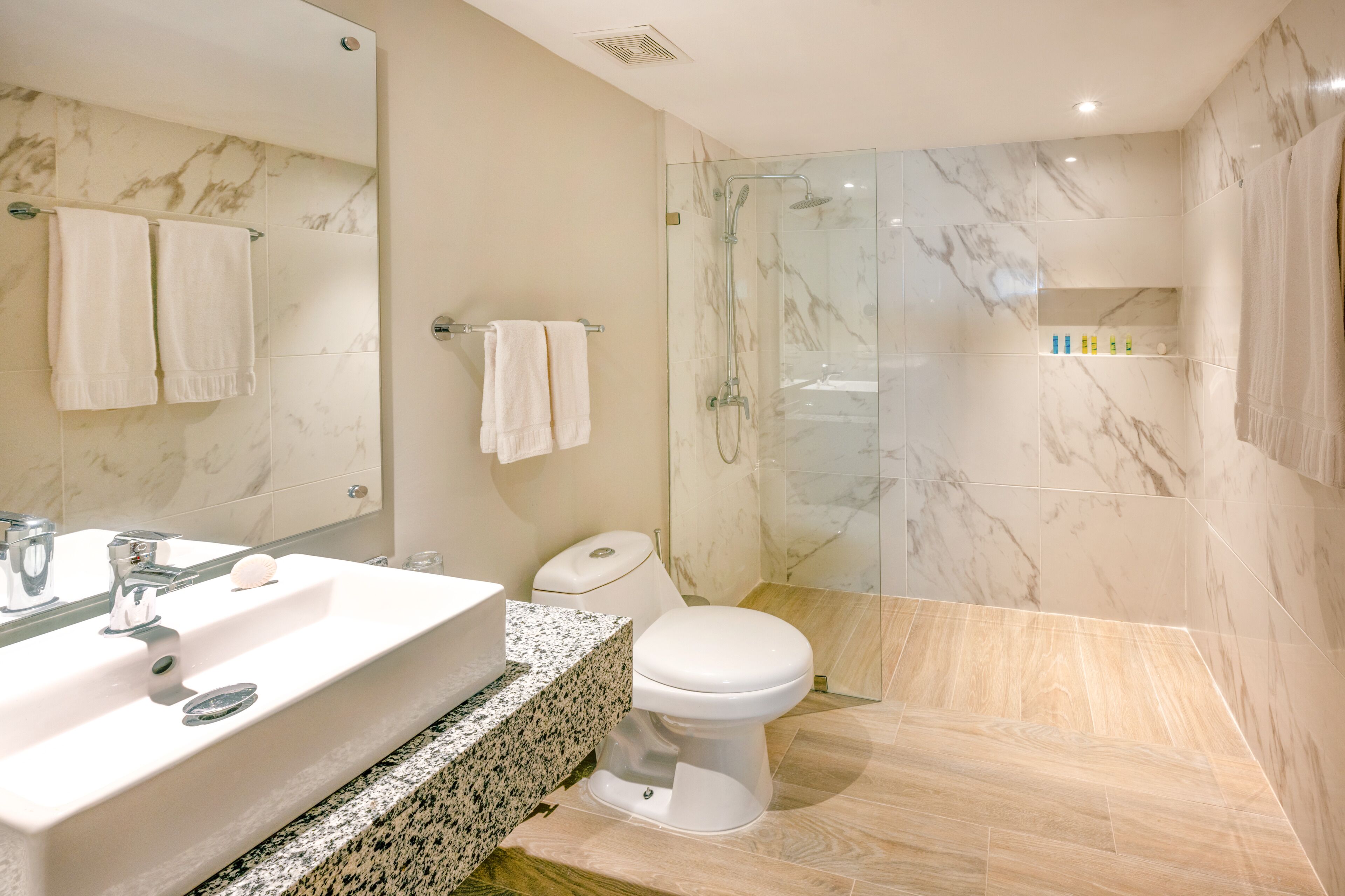 A modern bathroom with a marble sink, a toilet, and a glass-enclosed shower.