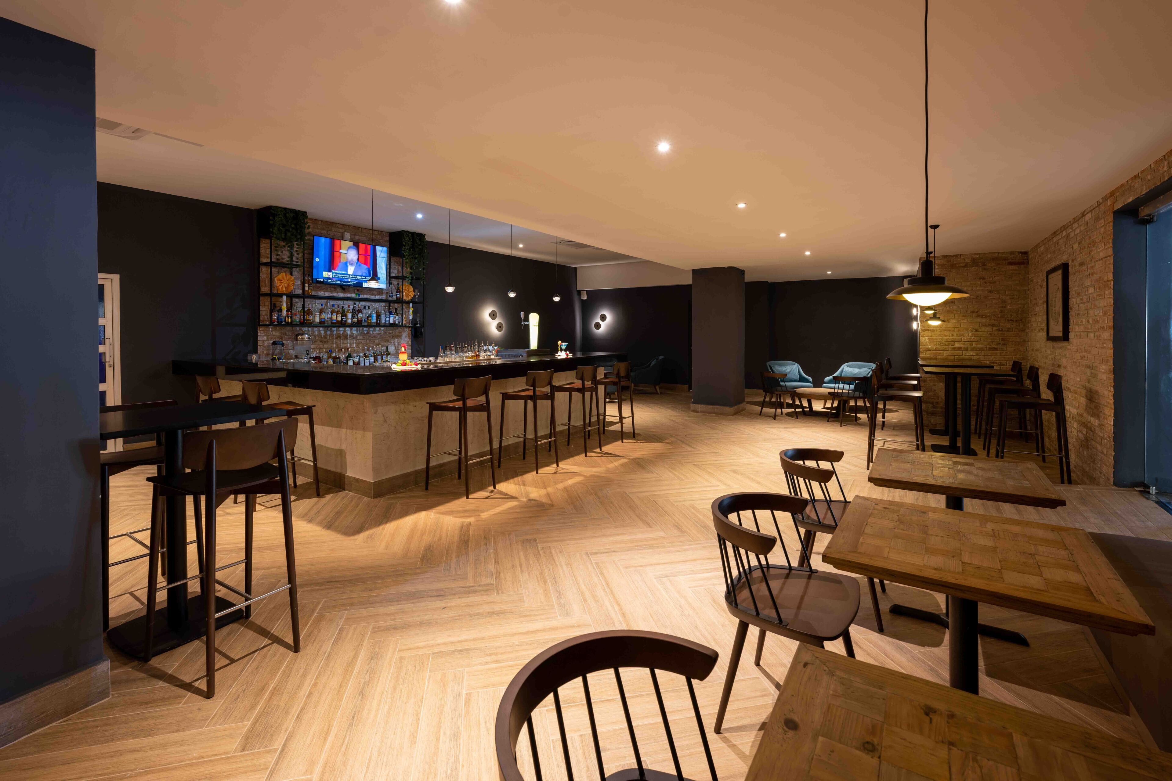A modern bar area with a television, bar stools, and wooden tables.