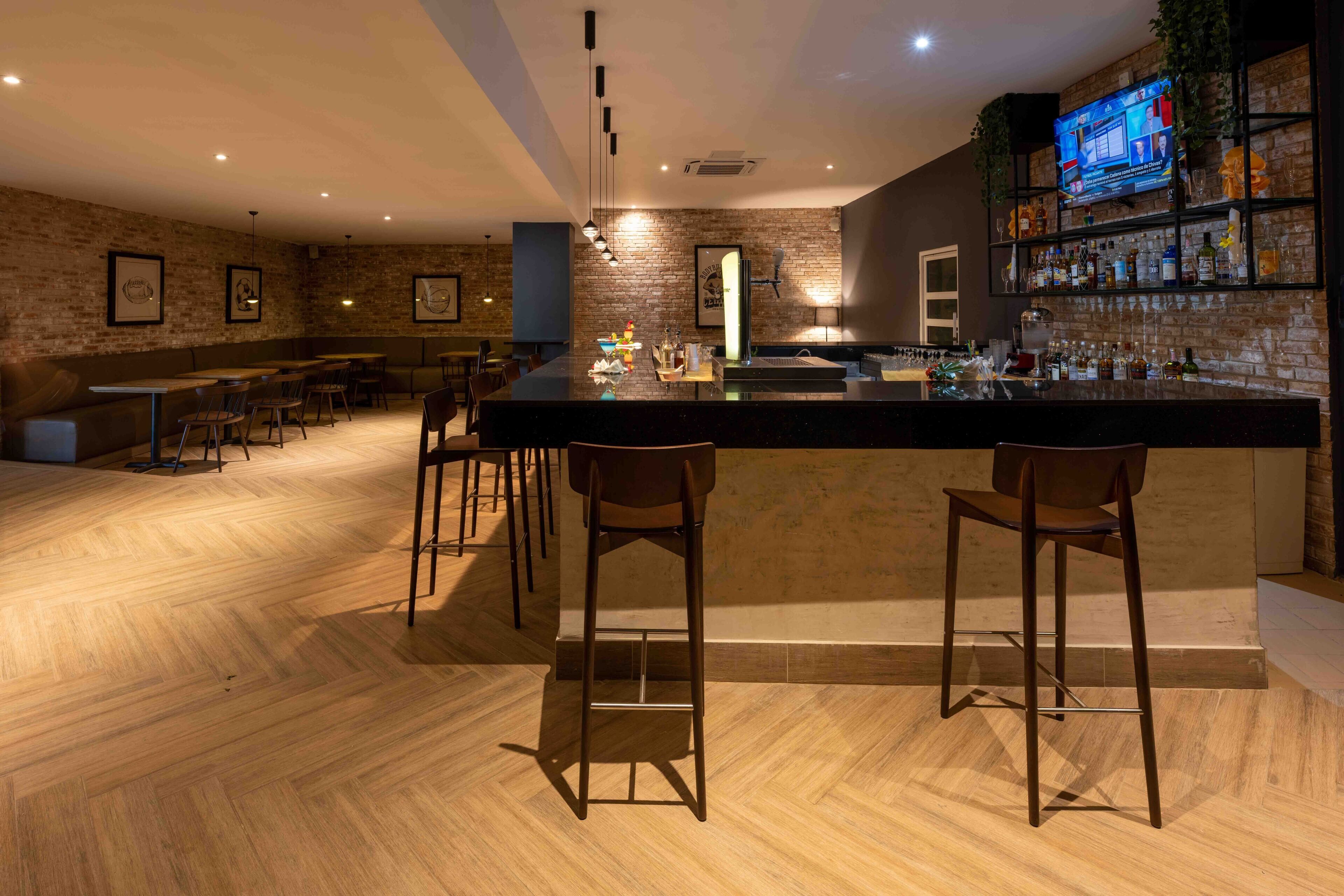 A bar area with a long counter, multiple stools, and a television screen above the bar.