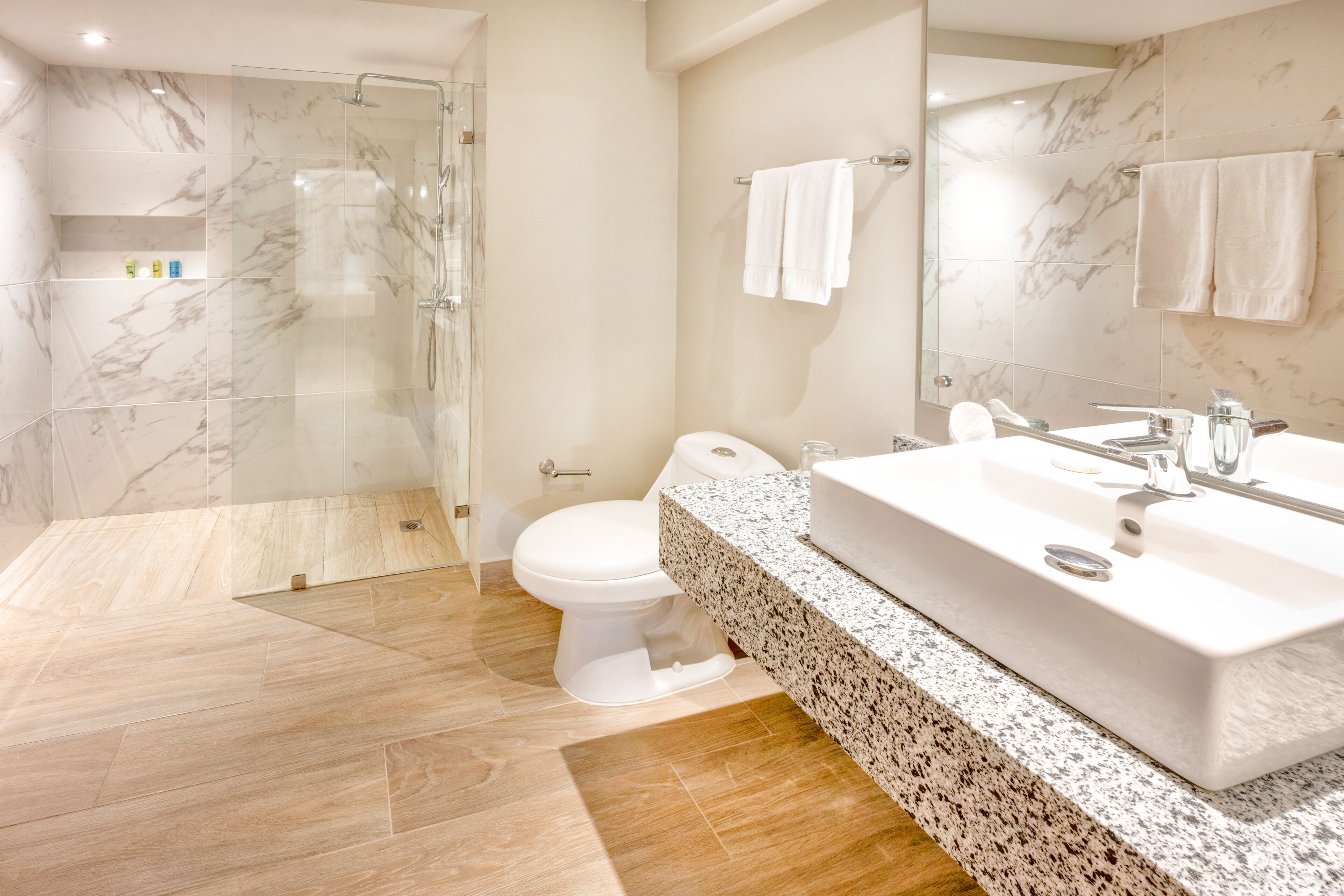 Ein modernes Badezimmer mit einer gläsernen Duschkabine, einer weißen Toilette und einem großzügigen Waschbecken mit Marmorplatte.