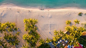 Luchtbeeld van een strand met helder turquoise water, een zandstrand en palmbomen.