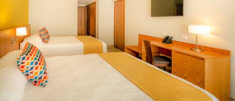 A hotel room with two beds, a desk, a chair, a TV, and a phone.