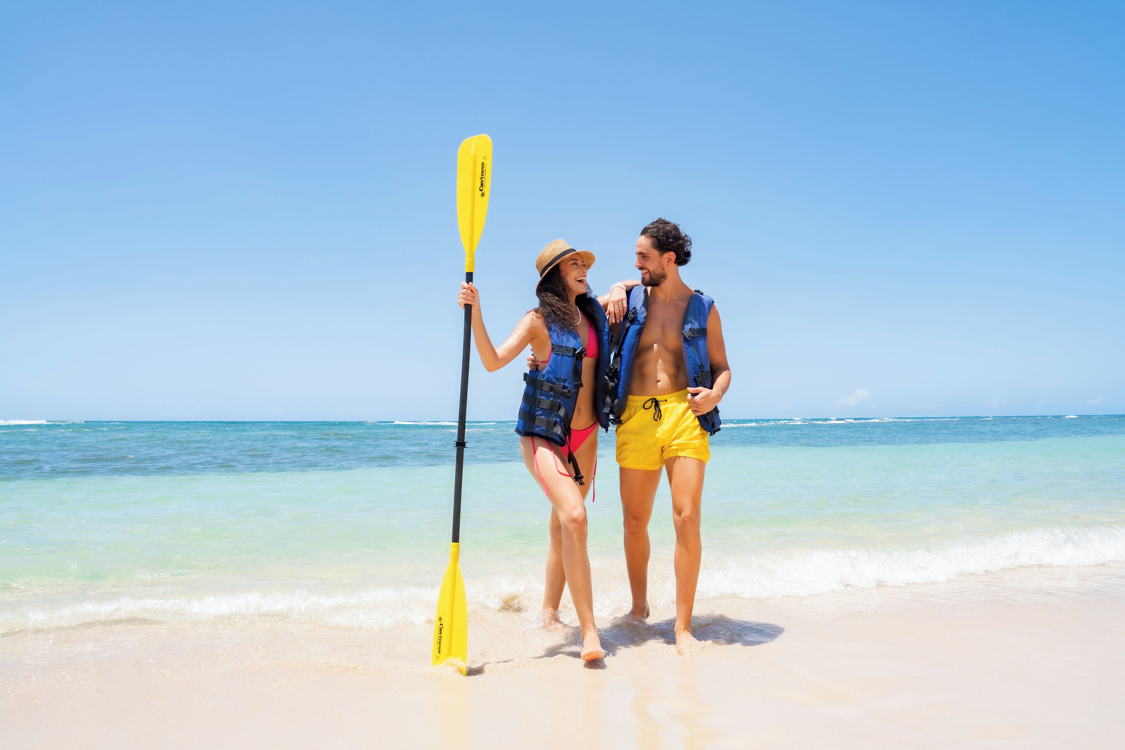 Una pareja caminando en la playa con una tabla de remo.