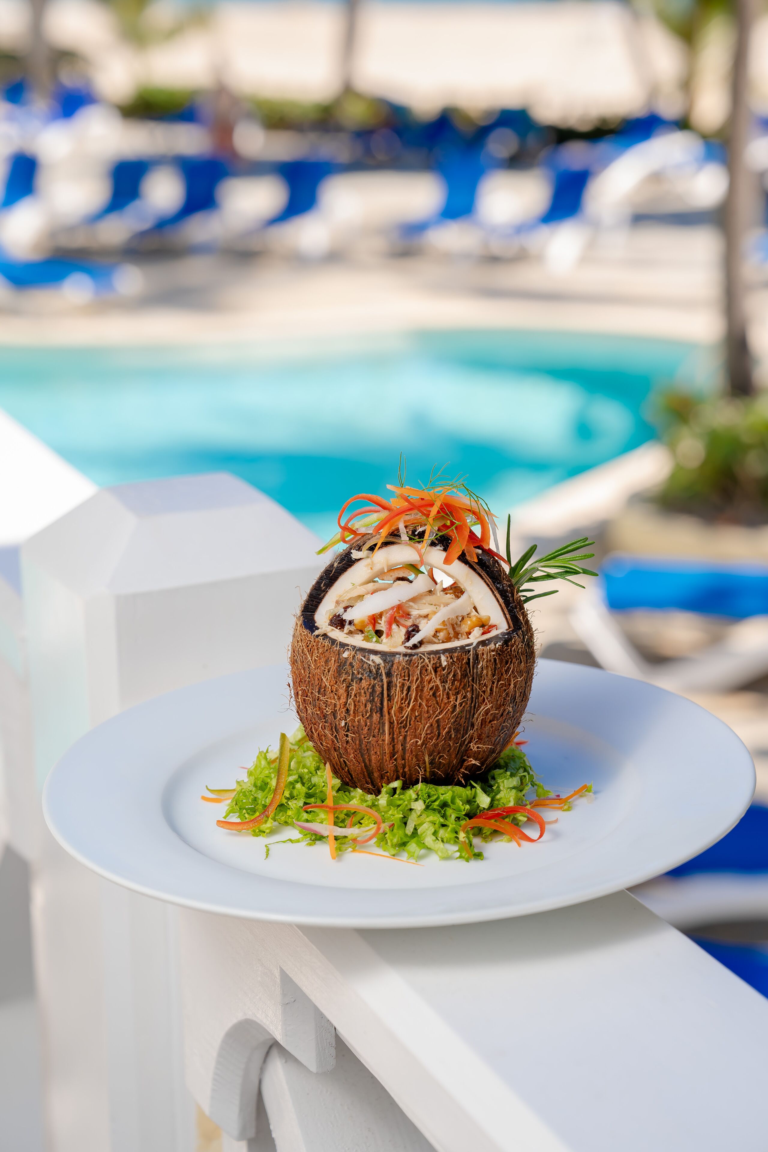A dish on a white plate with a pool and lounge chairs in the background.