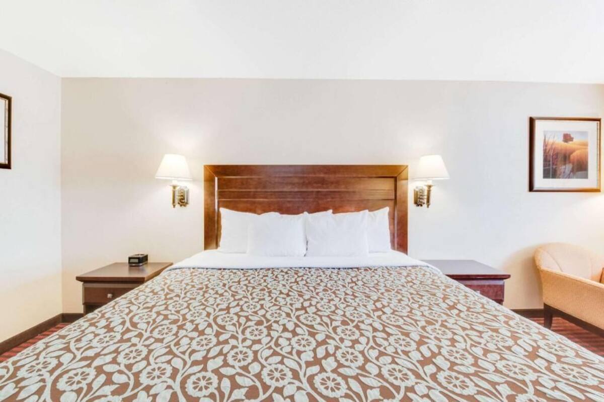 A hotel room with a large bed, two bedside lamps, a nightstand, a chair, and a framed picture on the wall.
