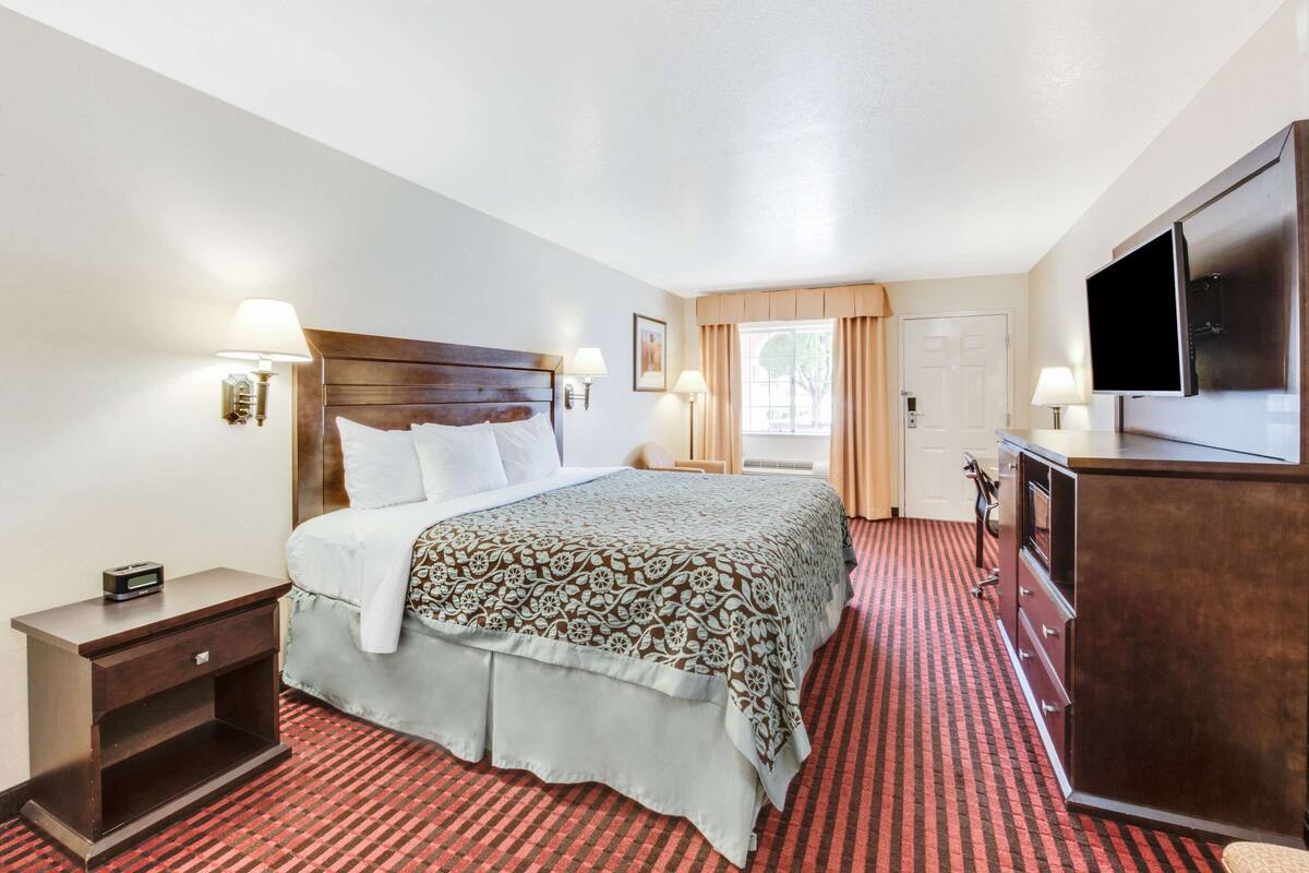 A hotel room with a large bed, a TV, a dresser, and a nightstand.