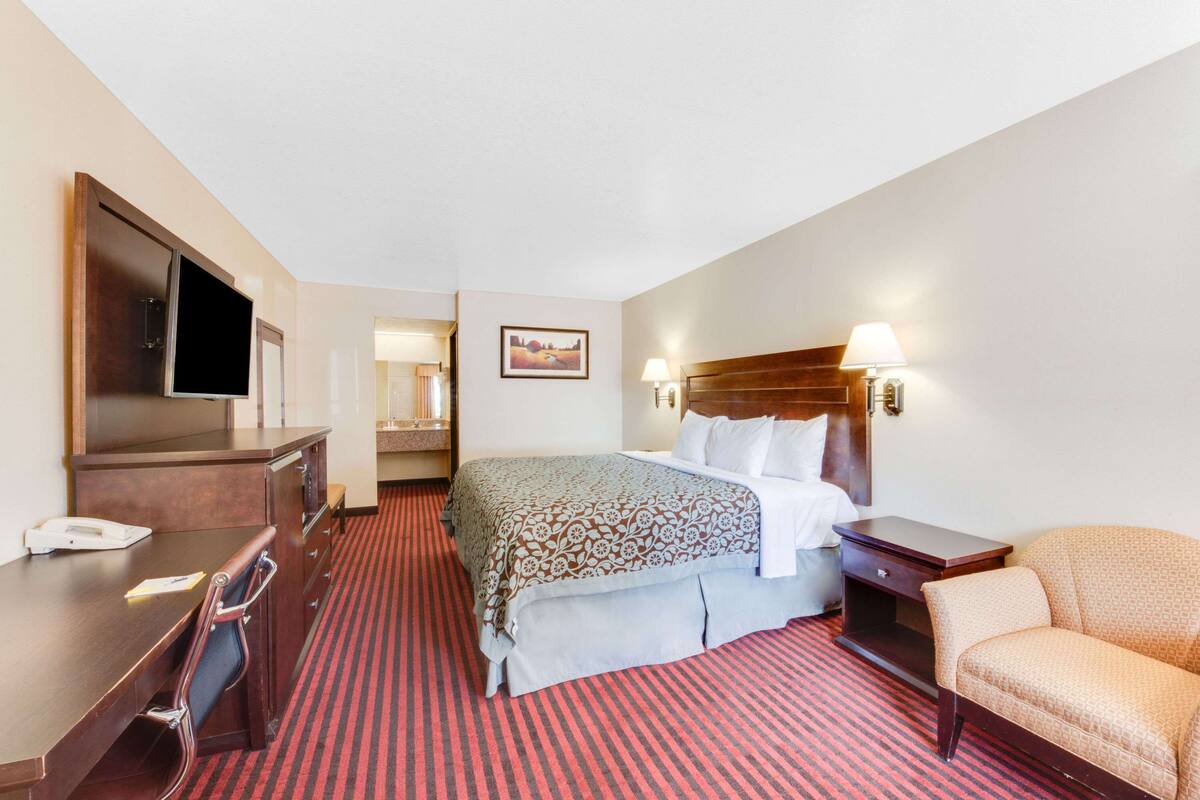 A hotel room with a bed, a desk, a chair, a TV, and a lamp.