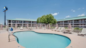 A Days Inn with a swimming pool, lounge chairs, and a large tree. - Days Inn by Wyndham Fort Stockton (Fort Stockton)