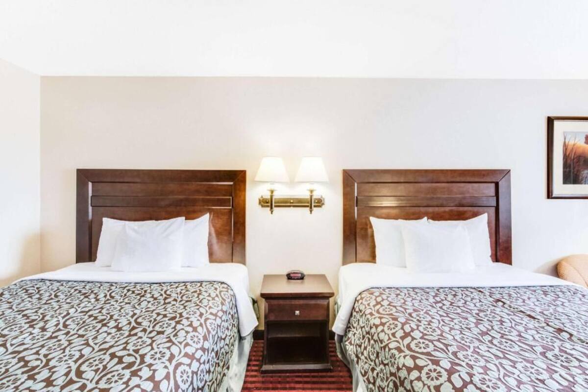 A hotel room with two beds, a nightstand, and a wall-mounted lamp.