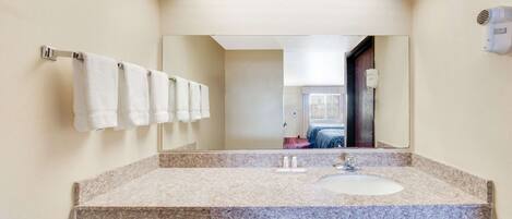 A modern bathroom with a granite countertop, a white sink, and a large mirror.